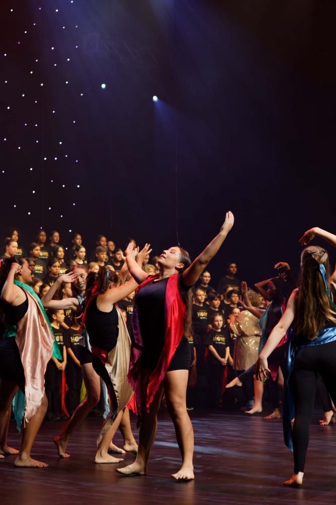 A group of young women are dancing on a stage in front of a choir.