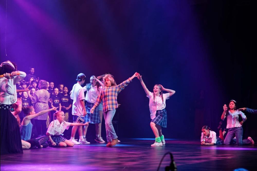 A group of young people are dancing on a stage holding hands.