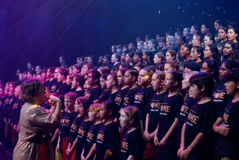 A woman is singing into a microphone in front of a large group of children.