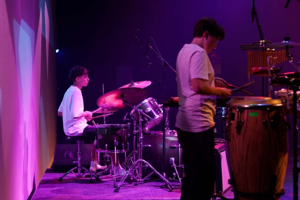 Two men are playing drums on a stage with purple lights behind them.