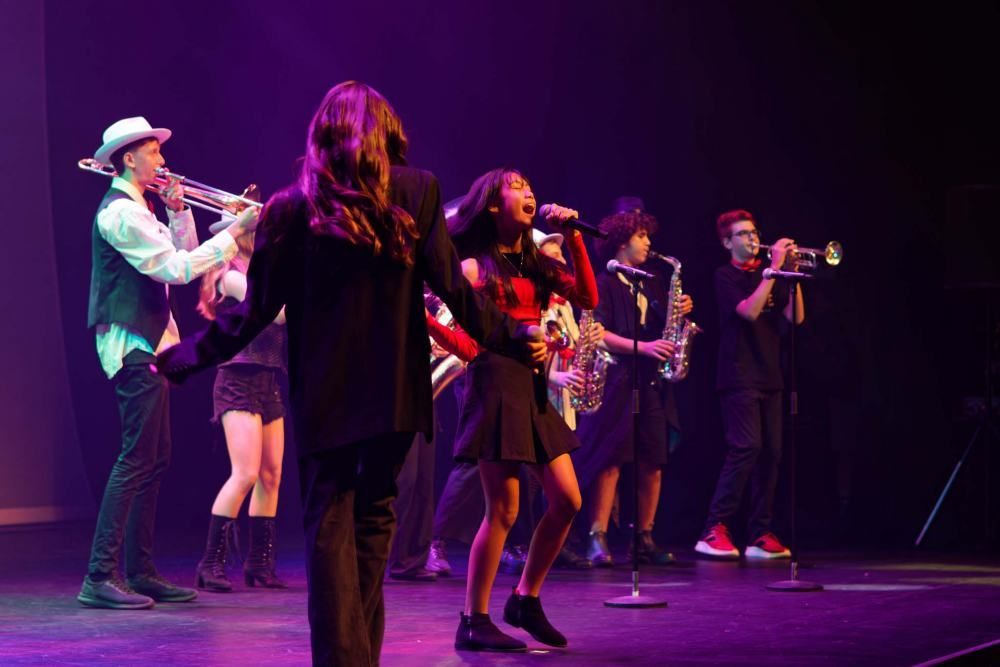 A group of people are standing on a stage playing instruments and singing into microphones.