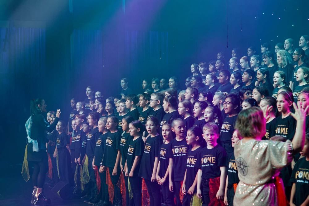 A large group of children are standing in a row on a stage.