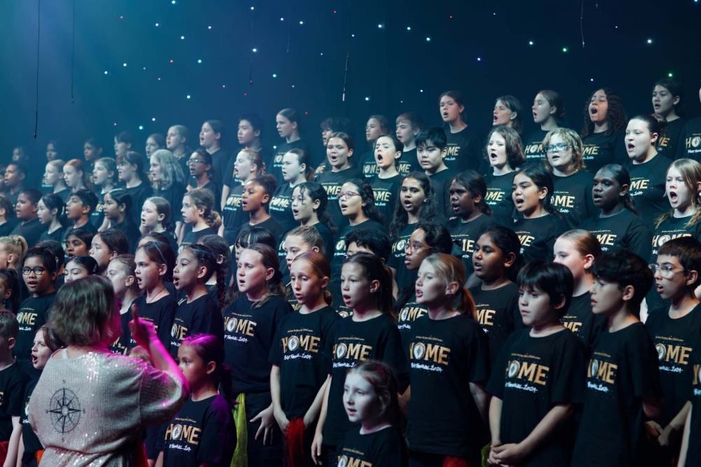 A large group of children are singing in a choir on a stage.