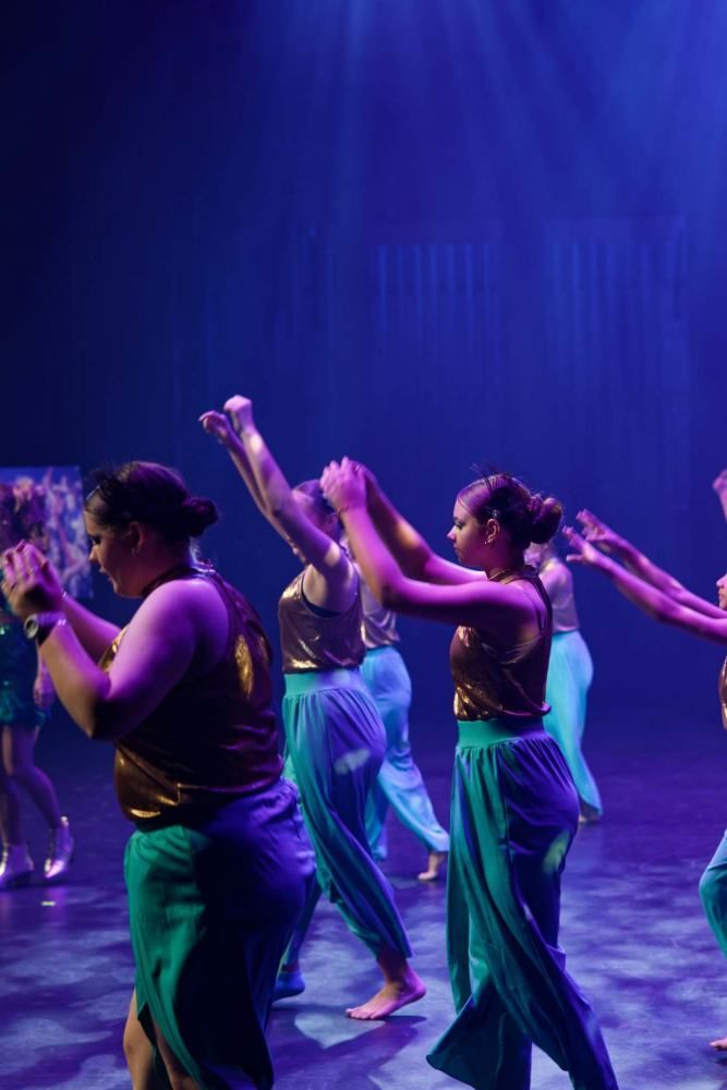 A group of women are dancing on a stage with purple lights.