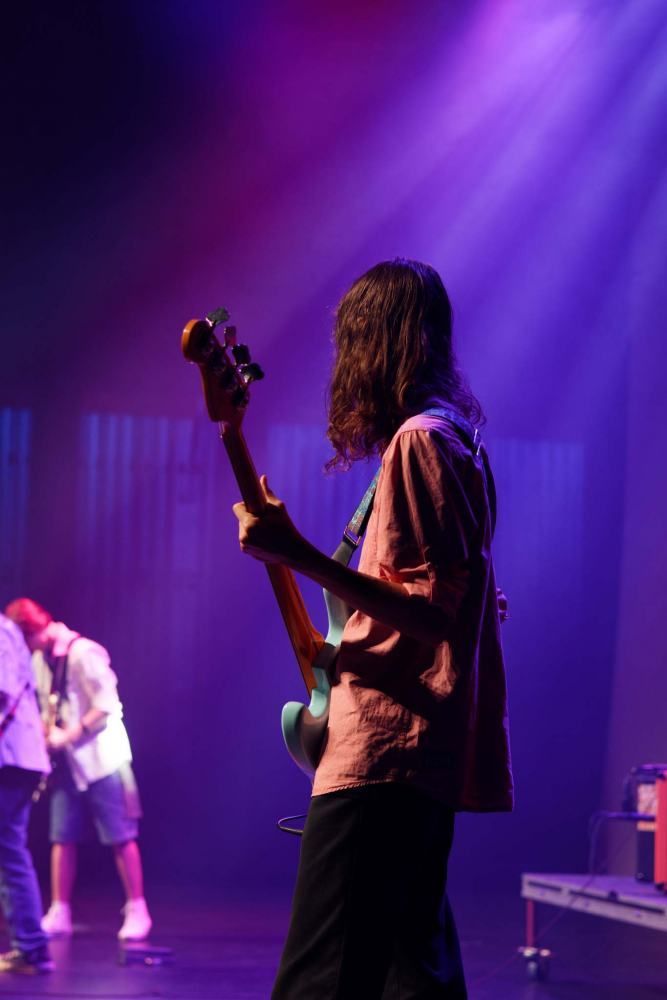 A man is playing a guitar on a stage with purple lights behind him.