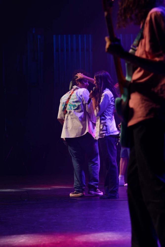 A group of people standing on a stage with a man playing a guitar