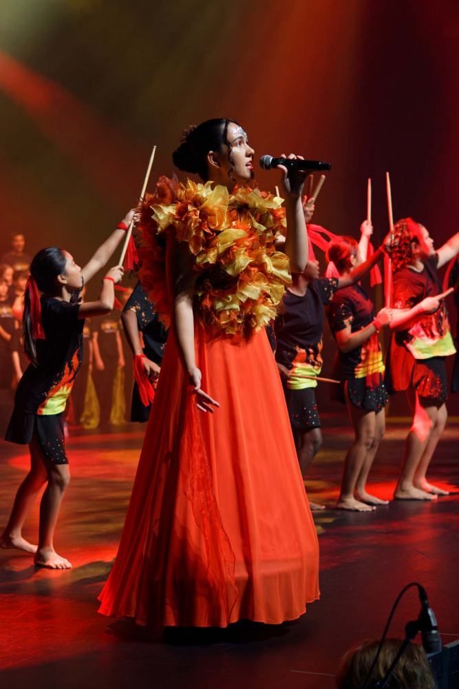 A woman in a red dress is singing into a microphone on a stage.