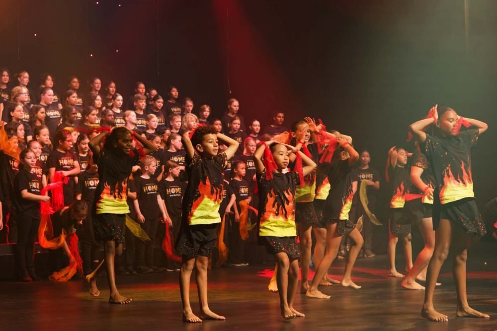 A group of children are dancing on a stage in front of a choir.