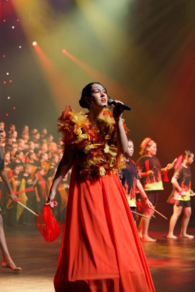 A woman in a red dress is singing into a microphone on a stage.