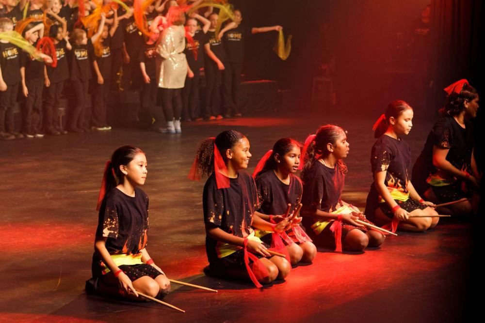 A group of young girls are sitting on the floor on a stage.