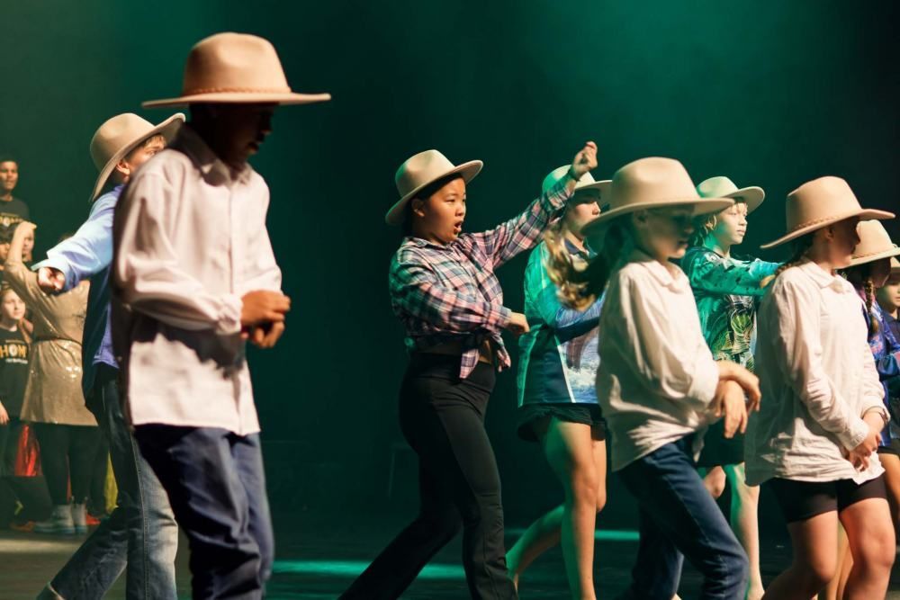 A group of children wearing cowboy hats are dancing on a stage.