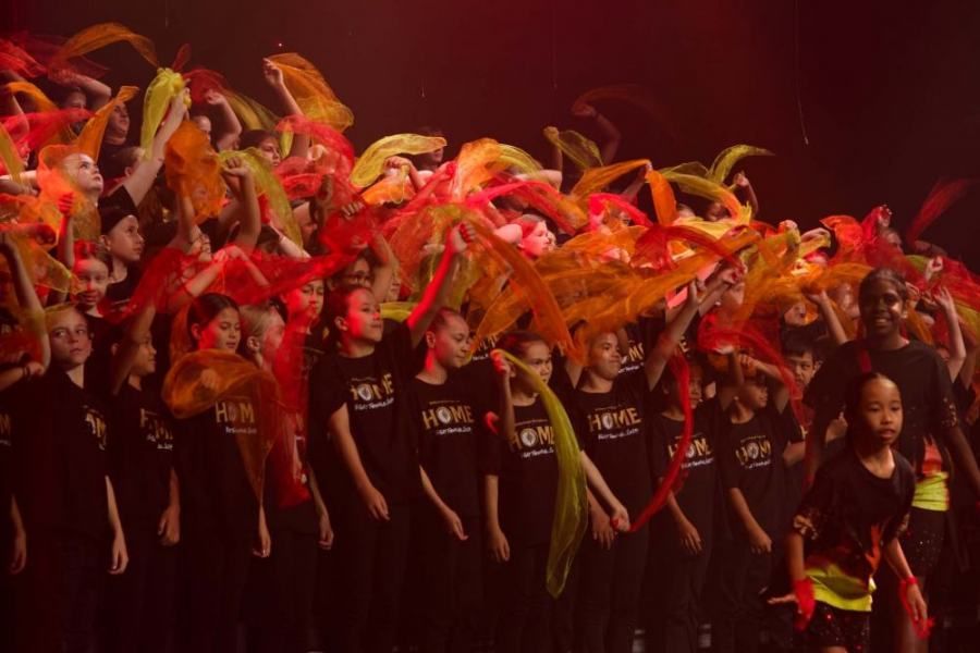 A large group of children are dancing on a stage.