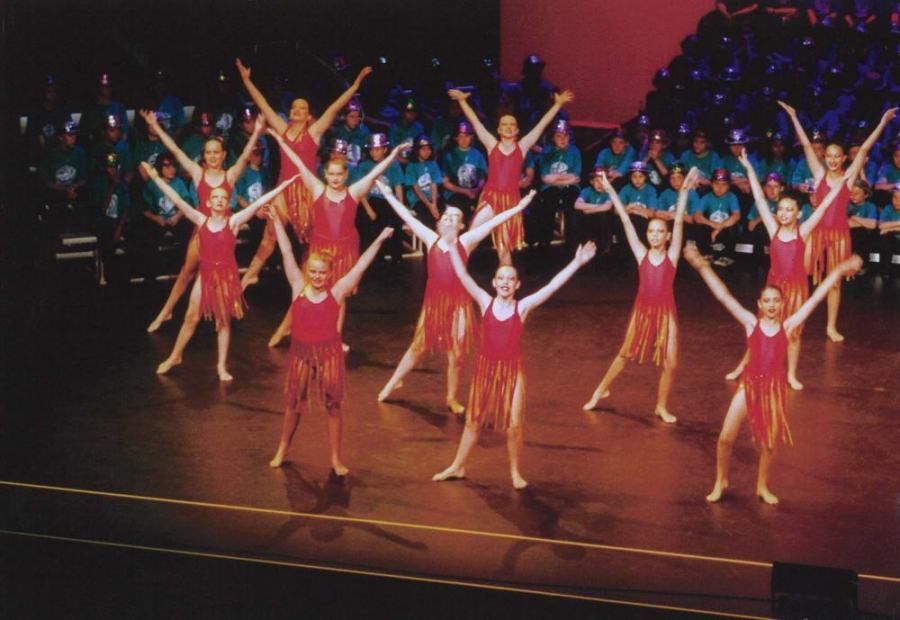 A group of young girls in red dresses are dancing on a stage