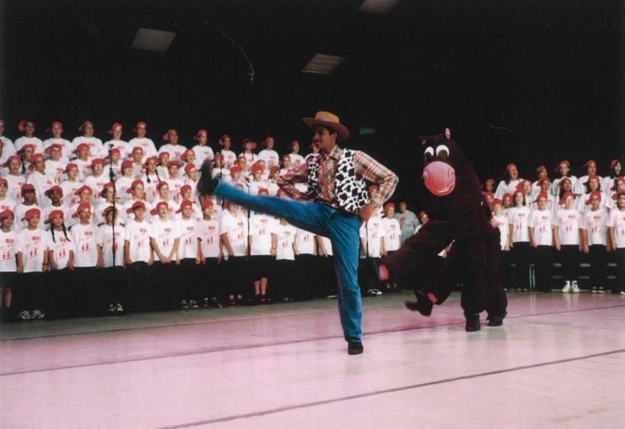 A man in a cowboy hat is kicking a balloon in front of a choir