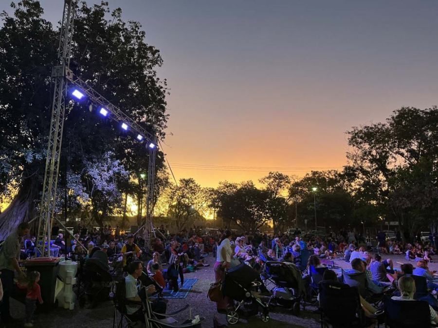 A crowd of people are gathered in a park at sunset