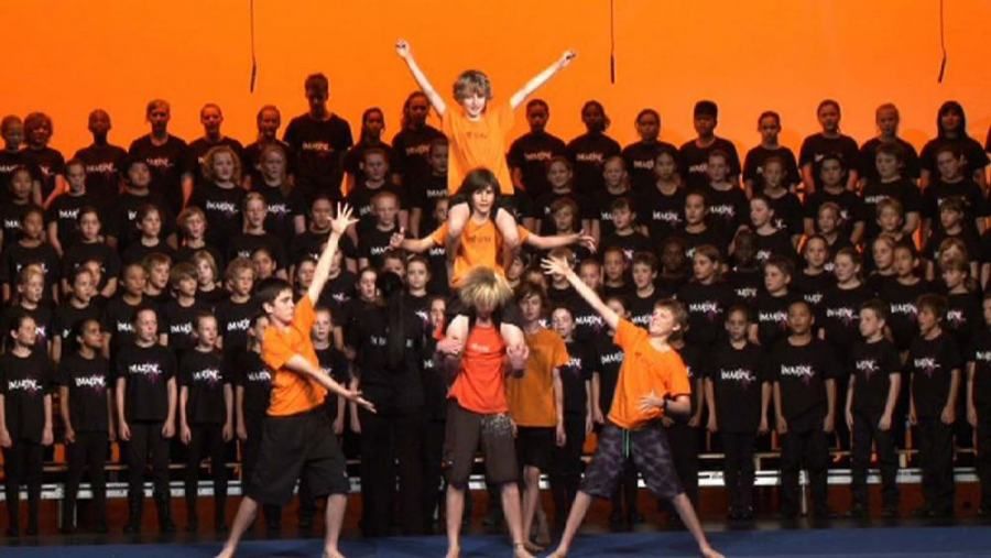 A group of children are performing in front of a large group of people