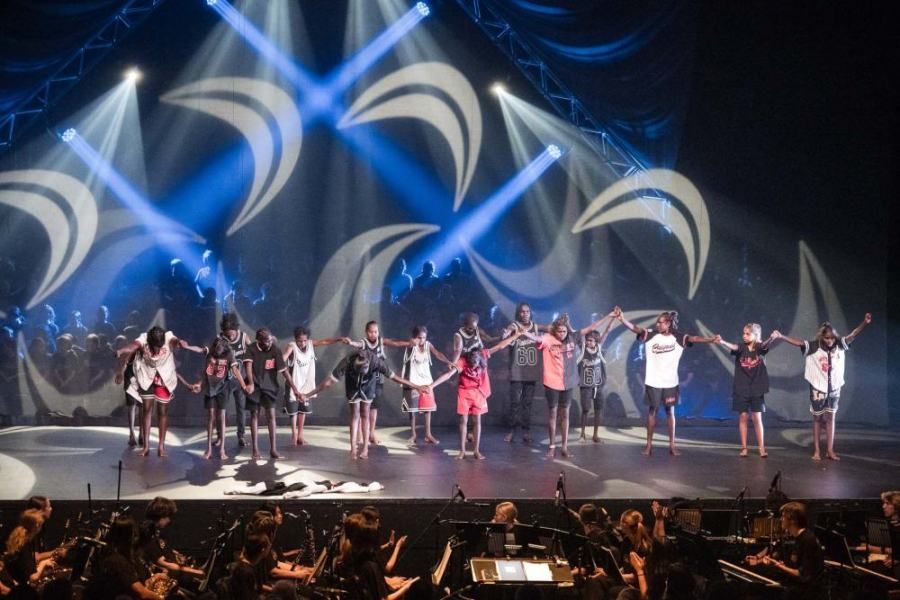 A group of people are standing on a stage holding hands