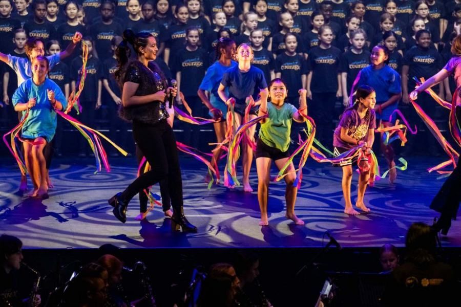 A group of children are dancing on a stage in front of a choir.