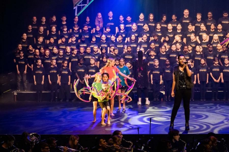 A man is singing into a microphone in front of a large choir.