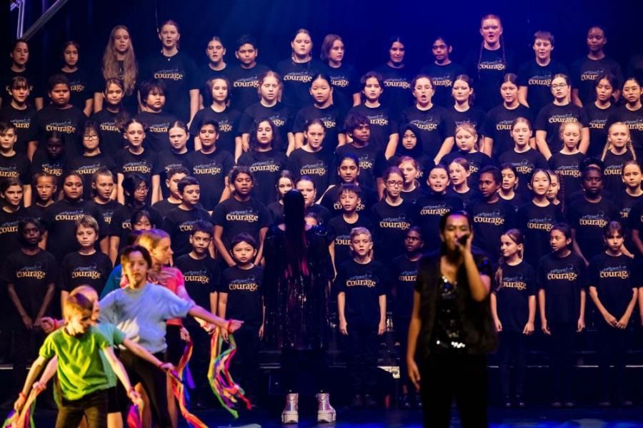 A group of children are dancing on a stage in front of a large choir.