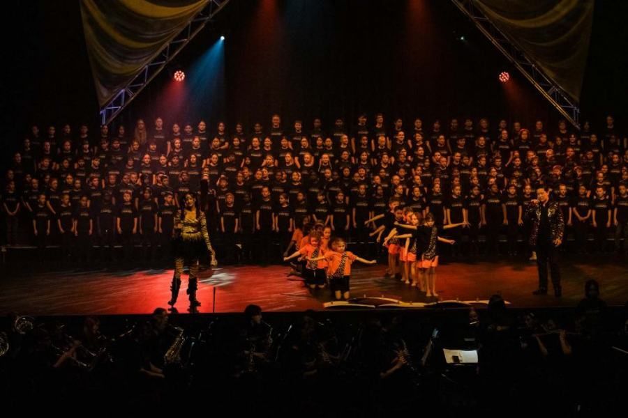 A large choir is performing on a stage in front of a crowd.