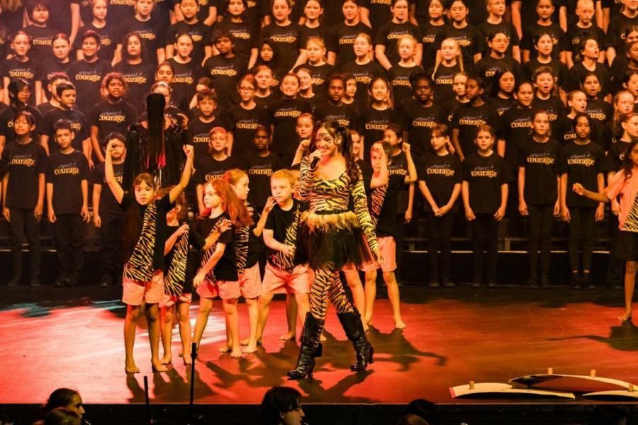 A woman is standing in front of a large choir on a stage.