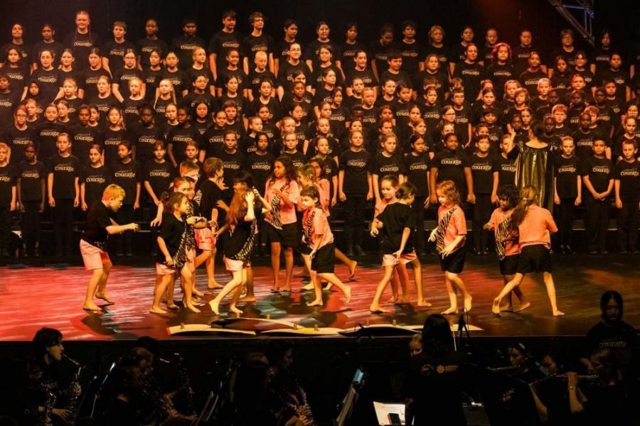 A group of children are dancing on a stage in front of a large choir.