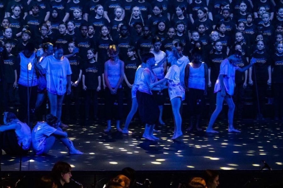 A group of children are dancing on a stage in front of a large audience.