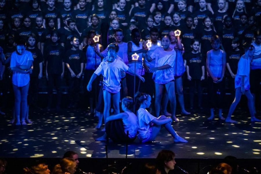 A group of children are performing on a stage in front of a crowd.