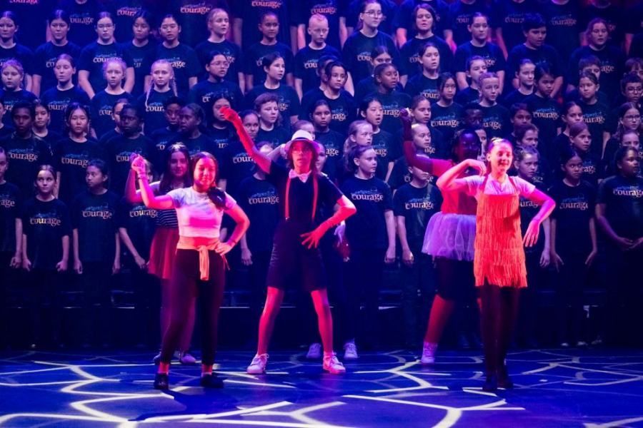 A group of young girls are dancing on a stage in front of a large choir.