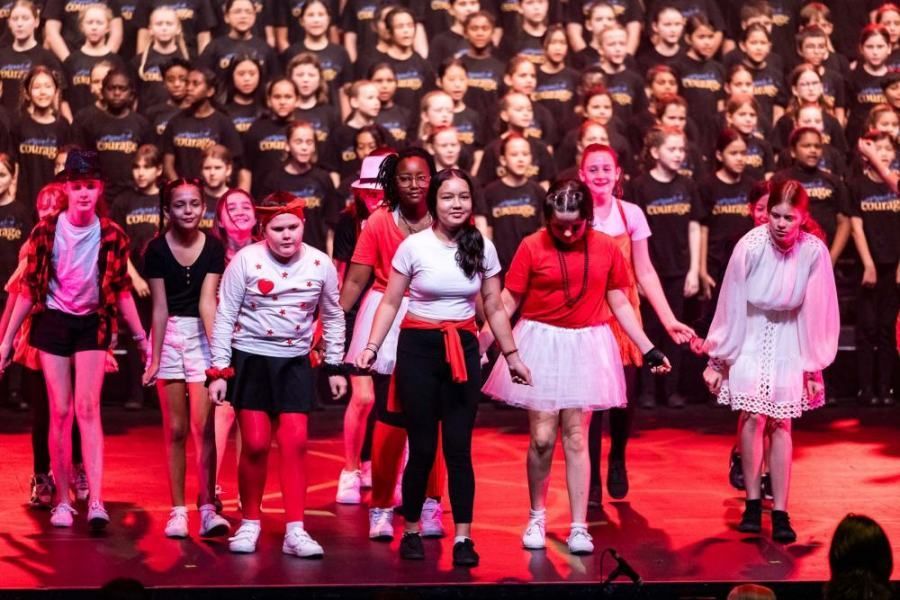 A group of young girls are standing on a stage holding hands.