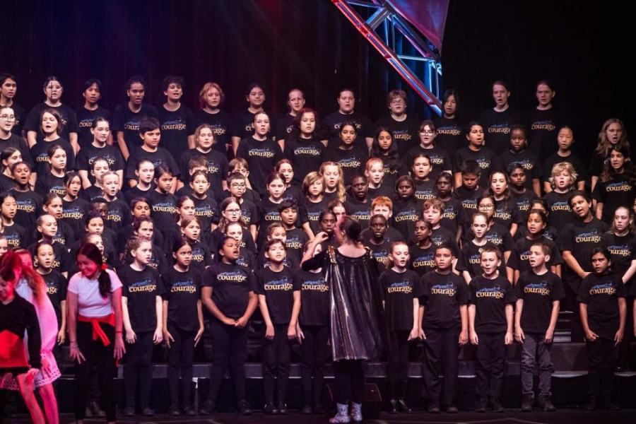 A large group of children are standing on a stage wearing black shirts