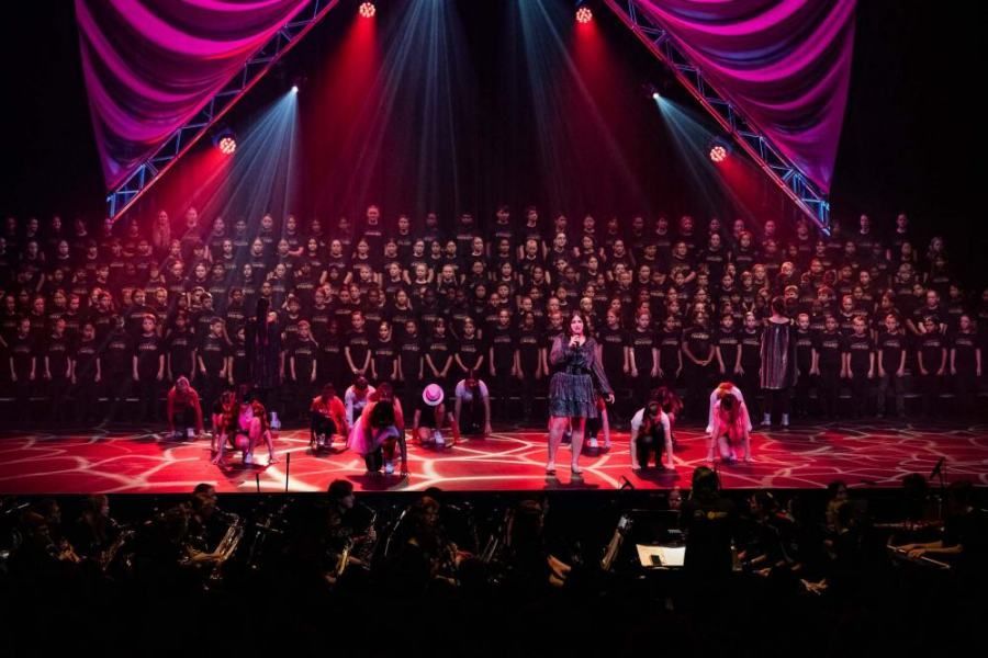 A large choir is performing on a stage in front of a crowd.