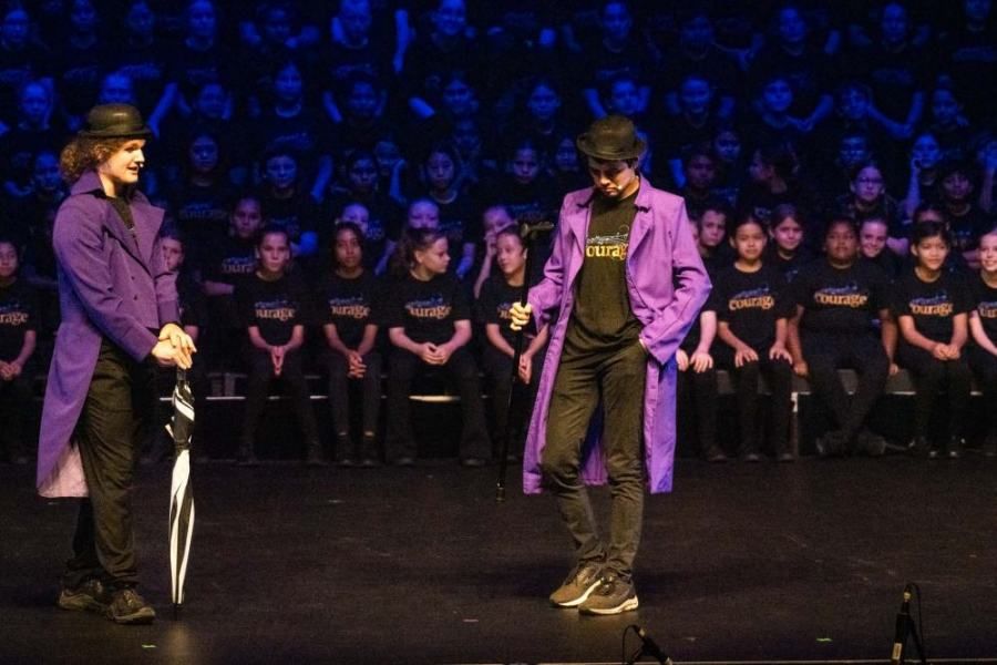 A man in a purple coat is standing next to a man in a black shirt on a stage.