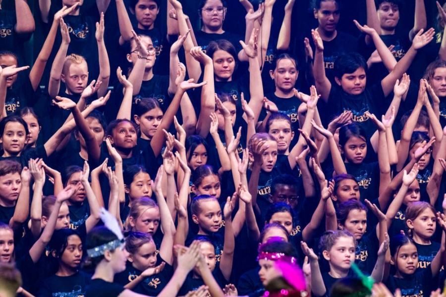 A large group of children are raising their hands in the air.