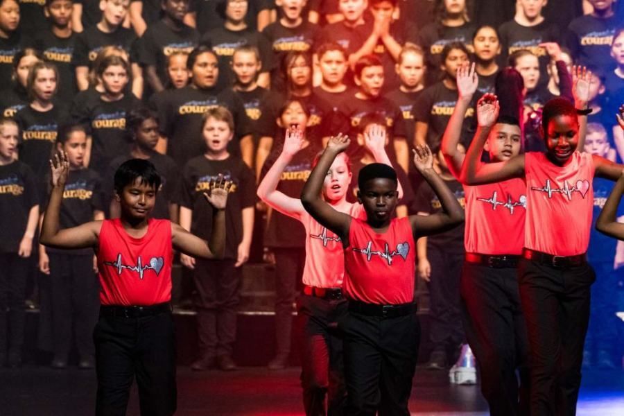 A group of children in red shirts are dancing on a stage.