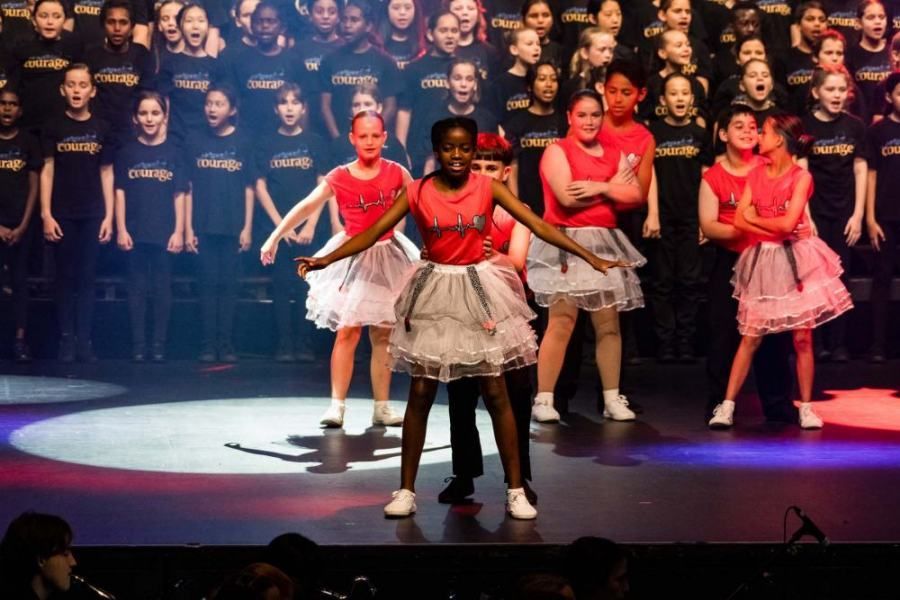 A group of young girls are dancing on a stage in front of a choir.