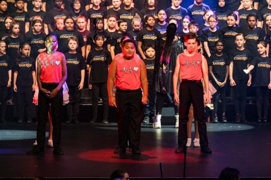 A group of children are standing on a stage in front of a large choir.