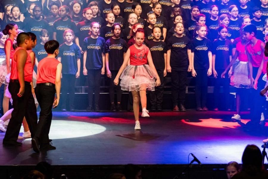 A group of children are dancing on a stage in front of a choir.