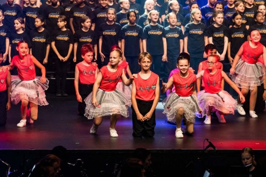 A group of young girls are dancing on a stage in front of a choir.