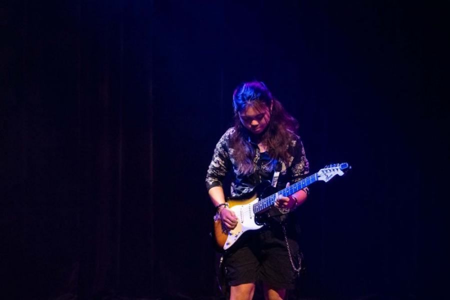 A woman is playing a guitar on a stage in a dark room.