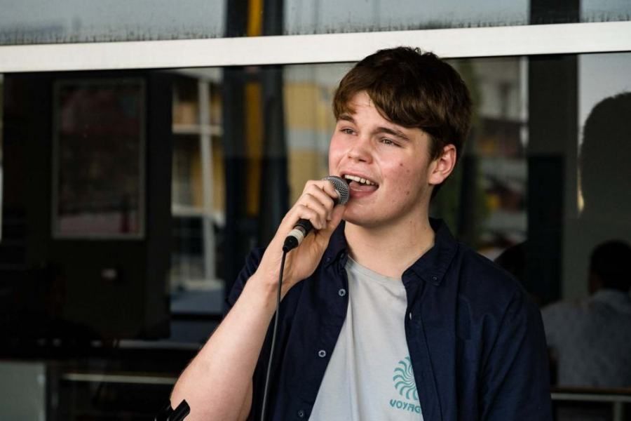 A young man is singing into a microphone in front of a window.