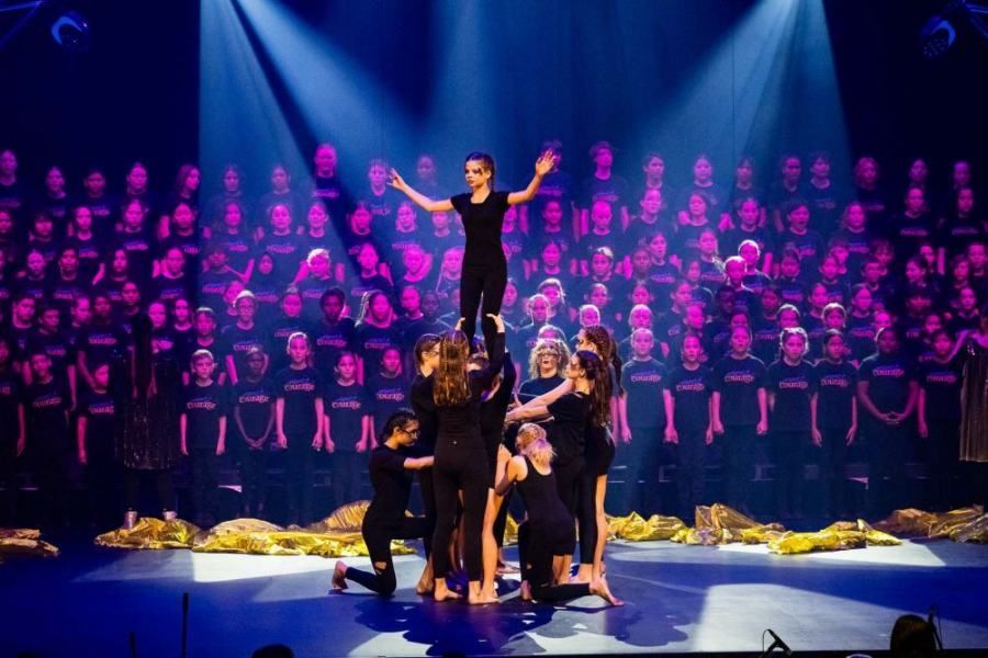 A group of children are performing on a stage in front of a choir.