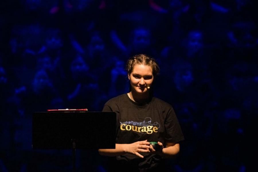 A woman in a courage shirt is standing in front of a laptop on a stage.
