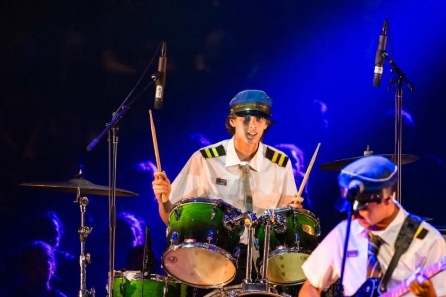 A man in a military uniform is playing drums on a stage.
