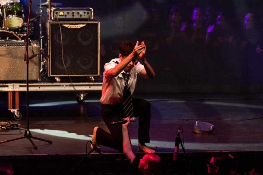 A man is kneeling down on a stage with a microphone in front of him