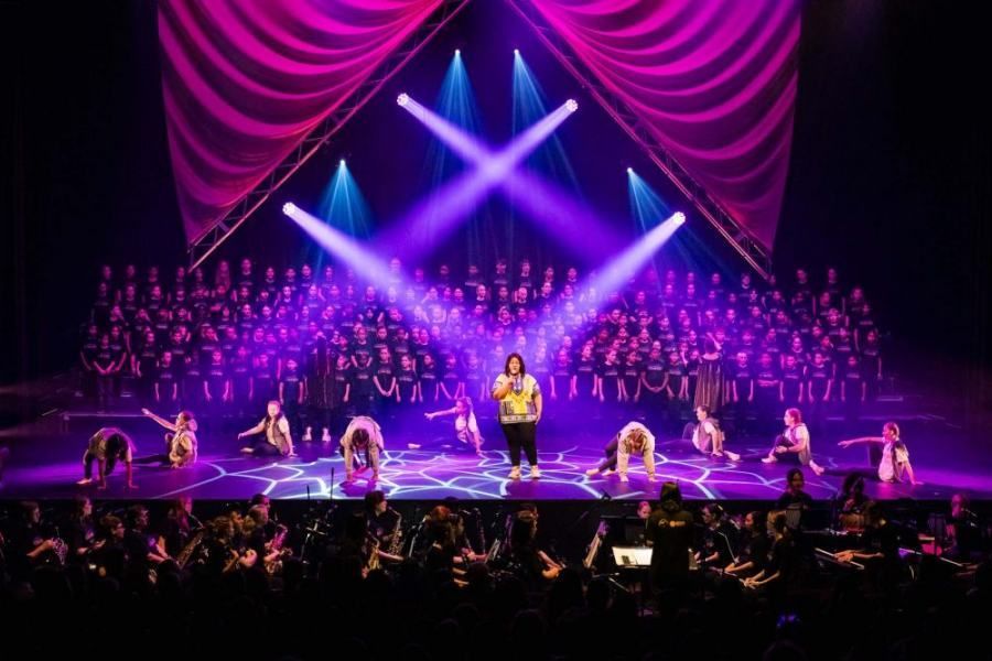 A group of people are dancing on a stage with purple lights