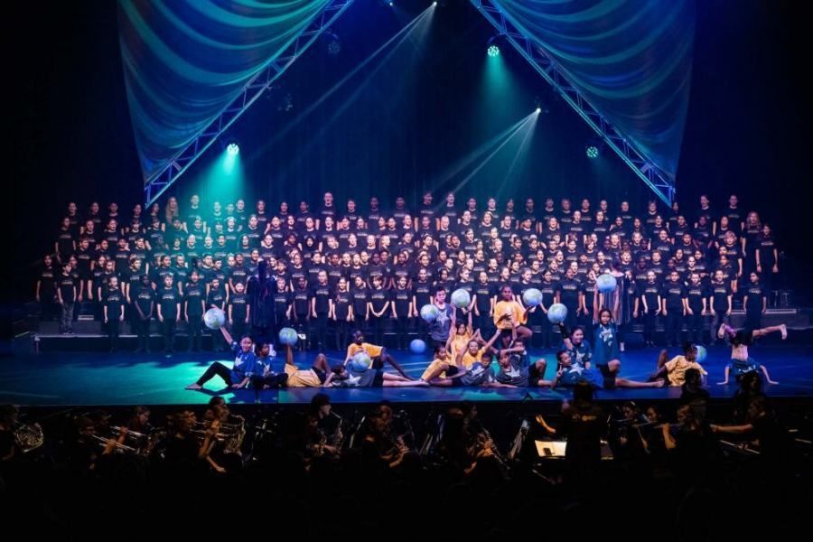 A large choir is performing on a stage in front of a crowd.