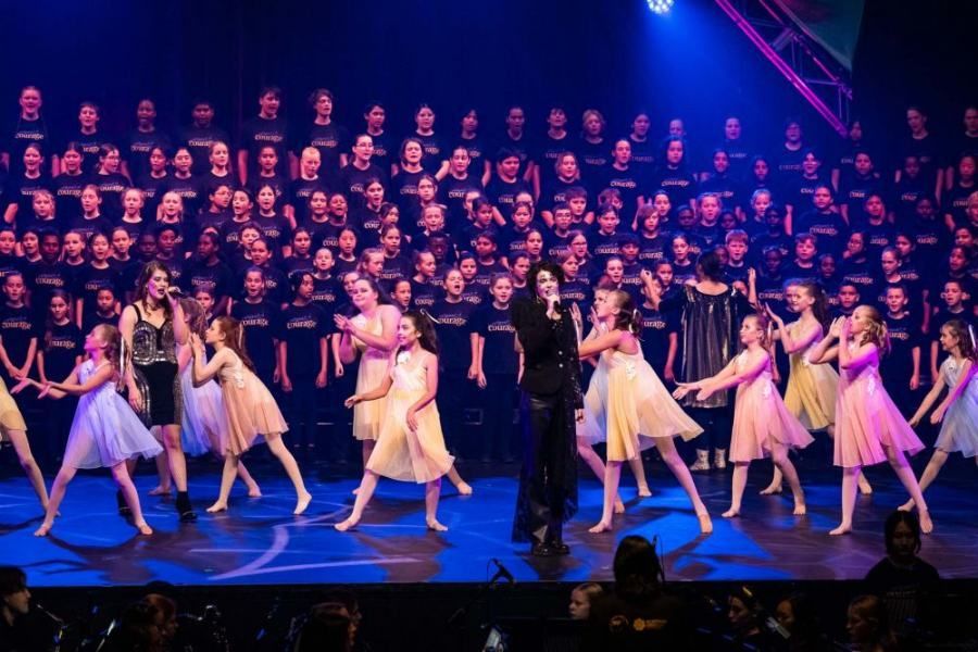 A group of young girls are dancing on a stage in front of a large choir.