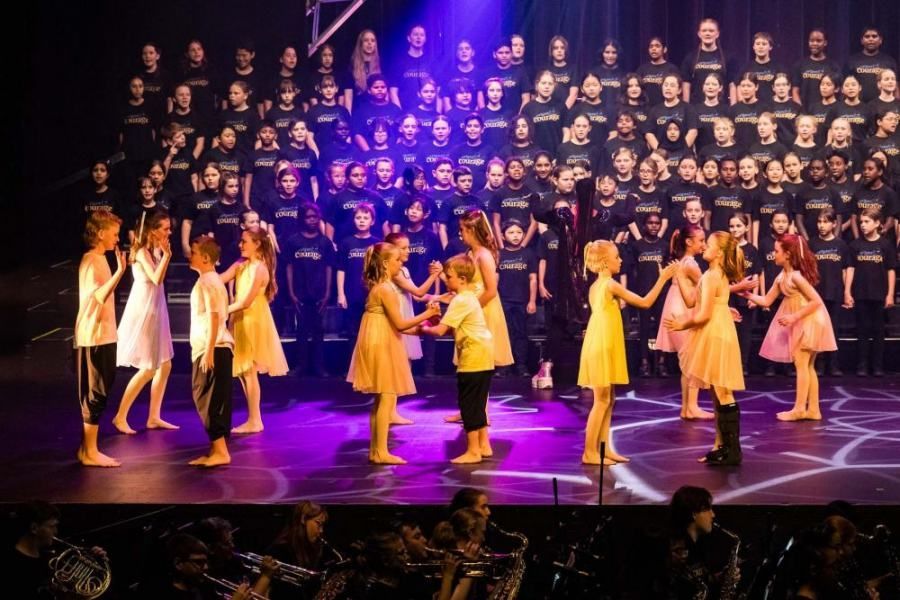 A group of children are dancing on a stage in front of a choir.